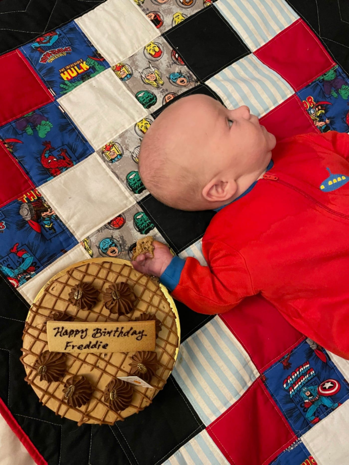 Baby reaches for a birthday cake while lying on a quilt