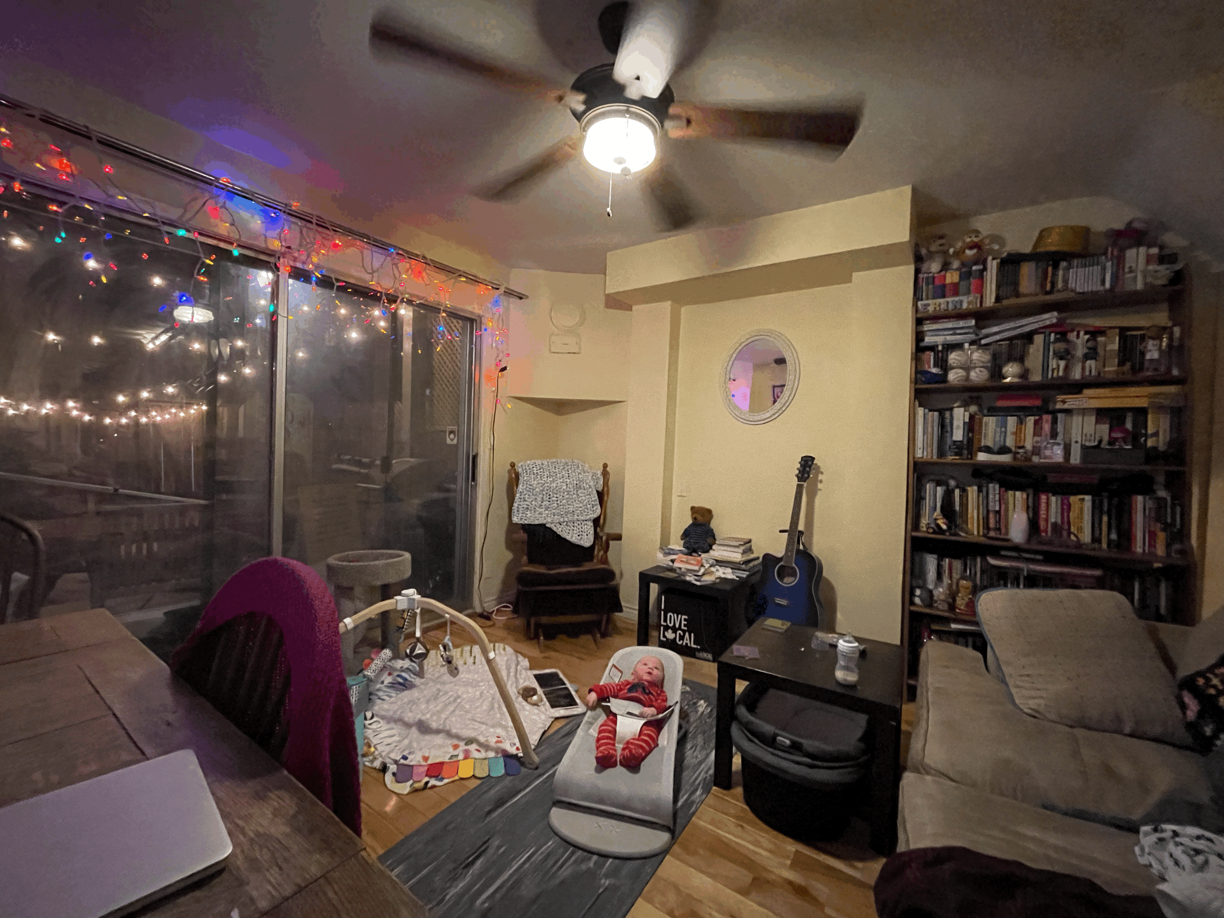 A photo of a baby in a bouncy chair staring at a ceiling fan.