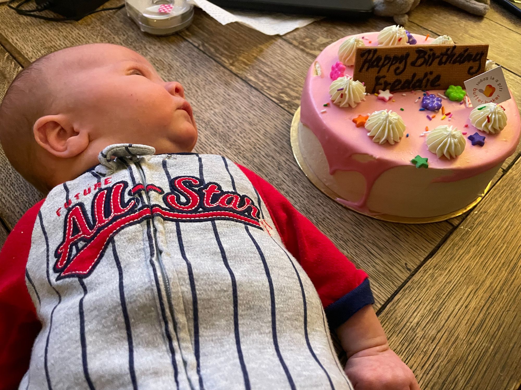 Freddie in a "Future All-Star" onesie, looking at a cake.