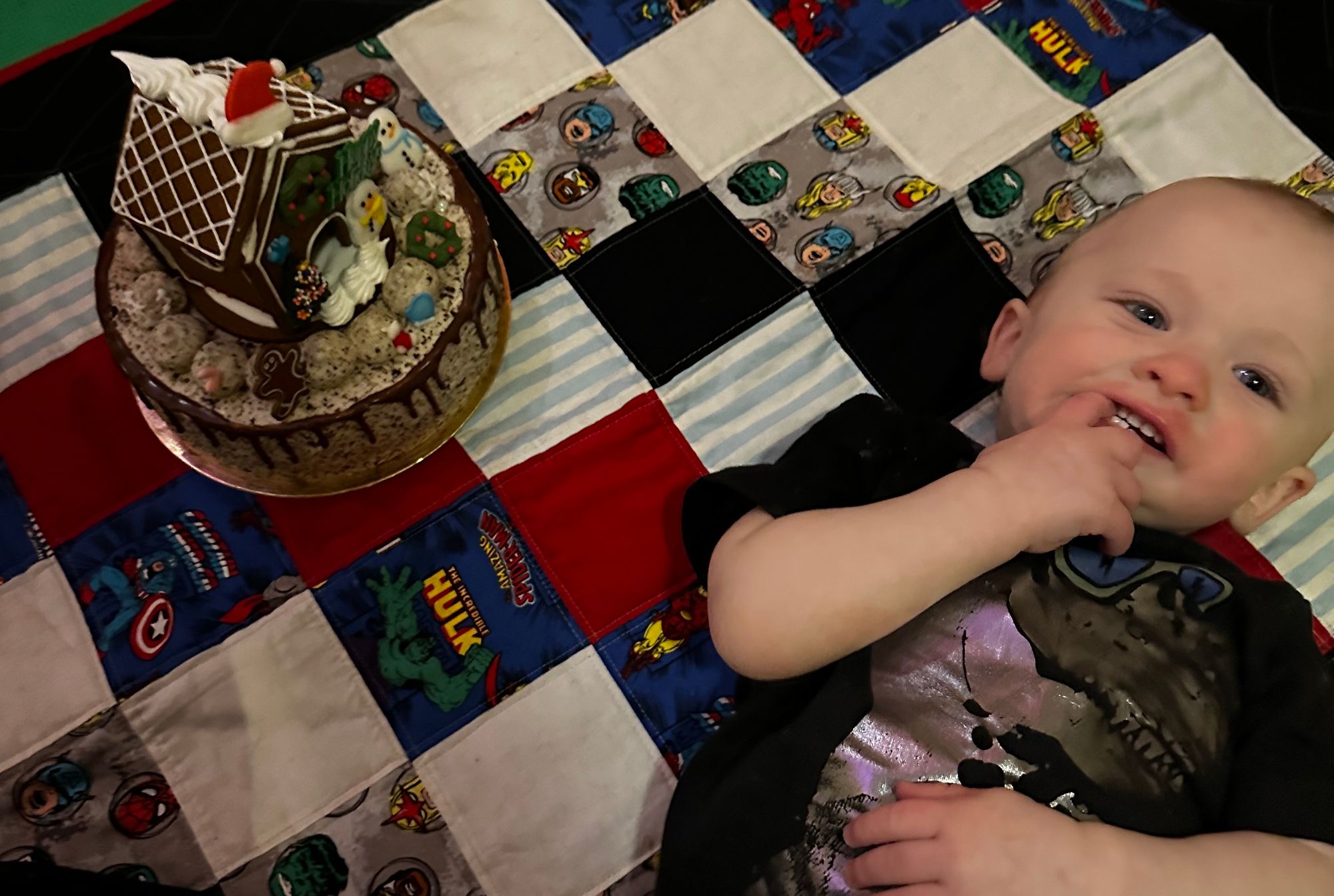 Freddie lying next to a cake adorned with a gingerbread house.
